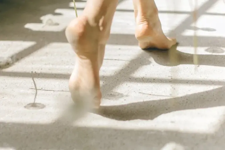Bare feet walking on a sunlit, textured surface with soft shadows