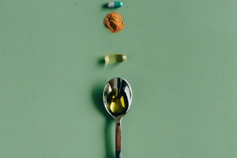 Spoon, capsules, and a small pile of calcium powder on a green background to illustrate calcium supplementation for bearded dragons.