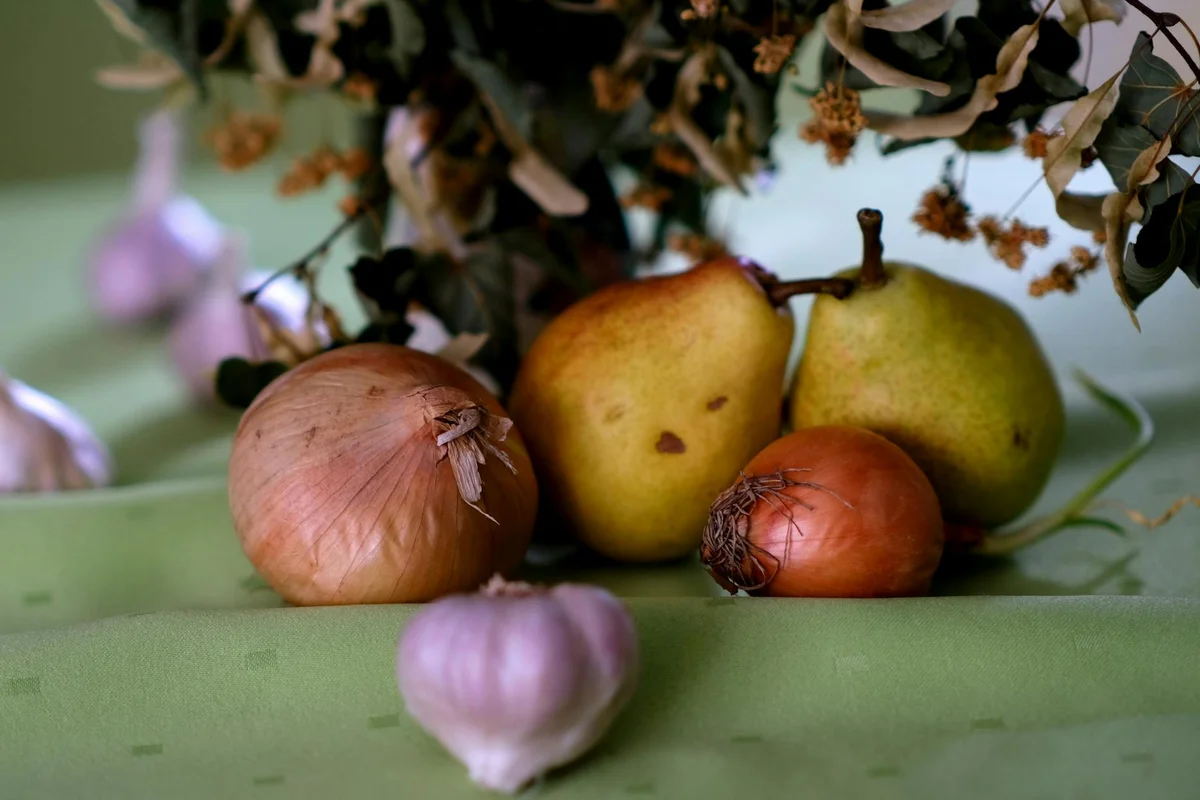 A still life image showing onions and pears on a green cloth, used to illustrate produce discussed in balancing a bearded dragon's diet.