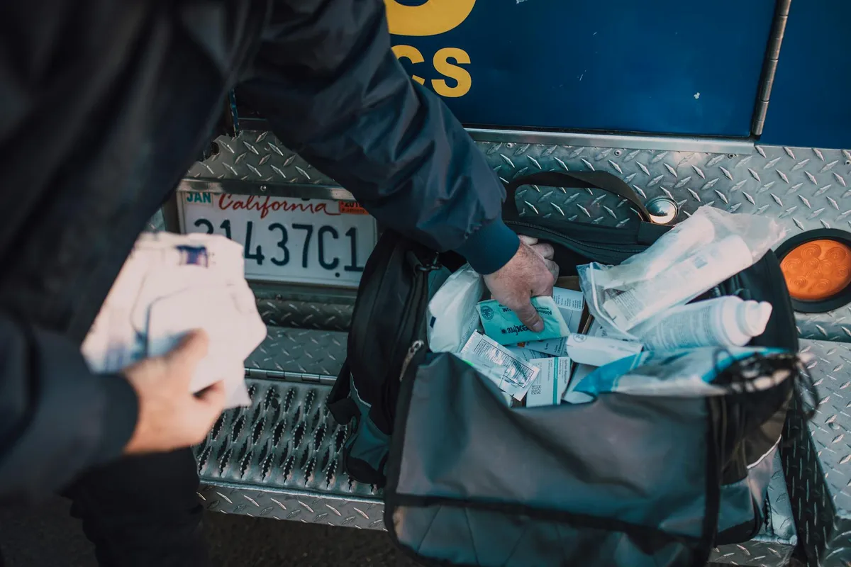 Person organizing a portable first aid kit with medical supplies in the back of a vehicle.