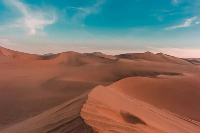 Desert landscape showing rolling orange sand dunes under a blue sky, illustrating heat and arid conditions.