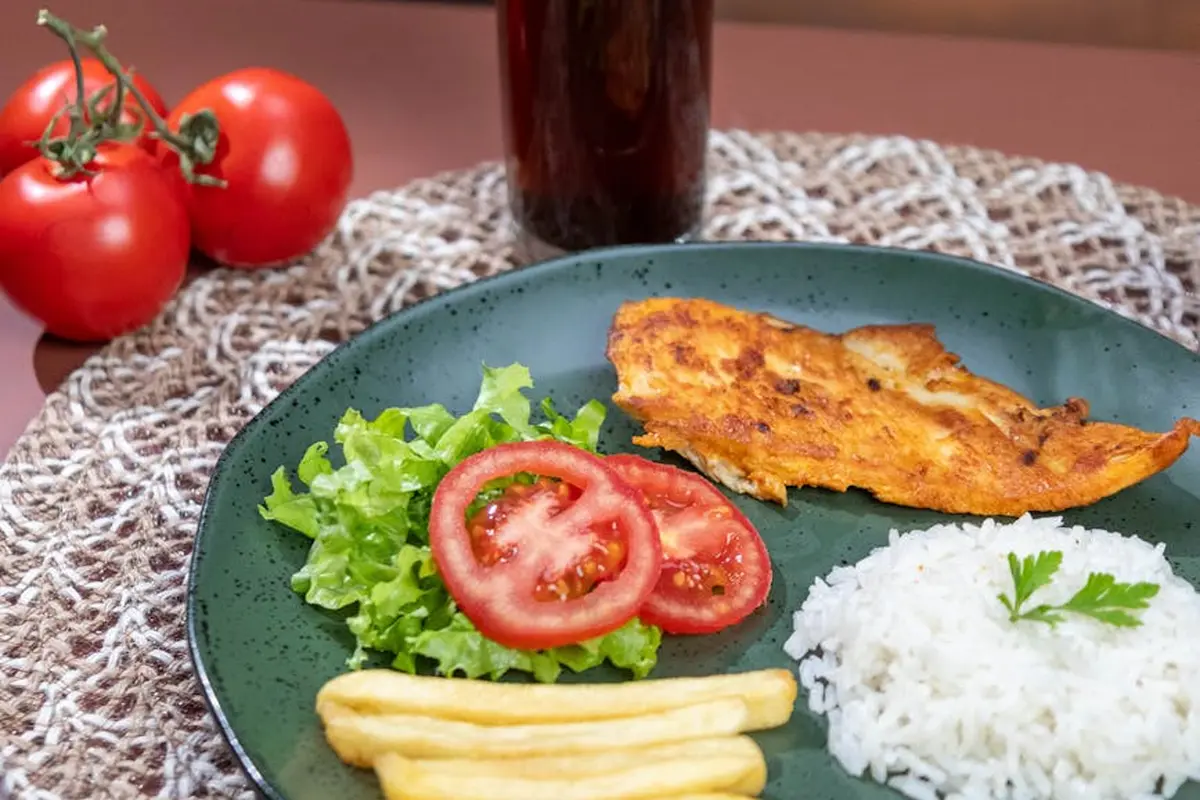 Plate with lettuce, tomato slices, white rice, and plantain chips on a blue plate; tomatoes on the vine in the background.