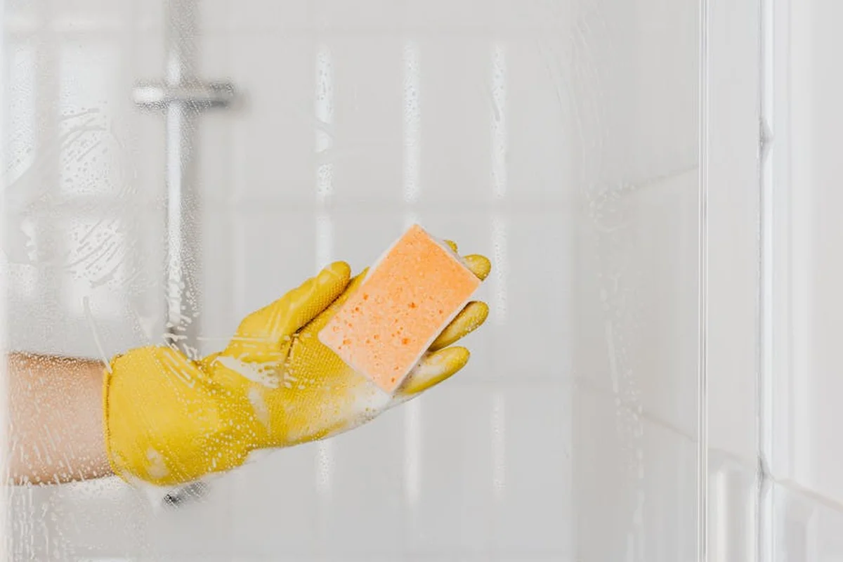 Gloved hand holding a pink sponge scrubbing a glass tank