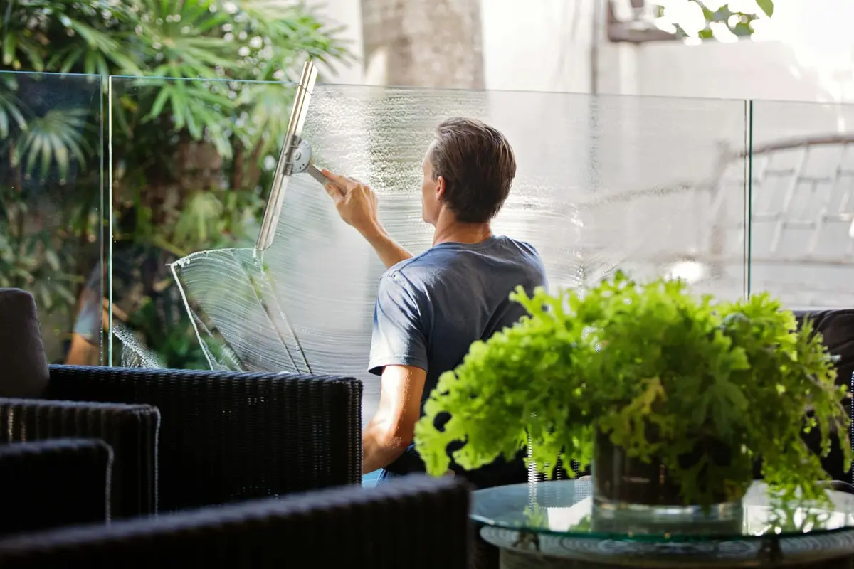 Adult cleaning a glass bearded dragon enclosure with a squeegee in a living room-style setting