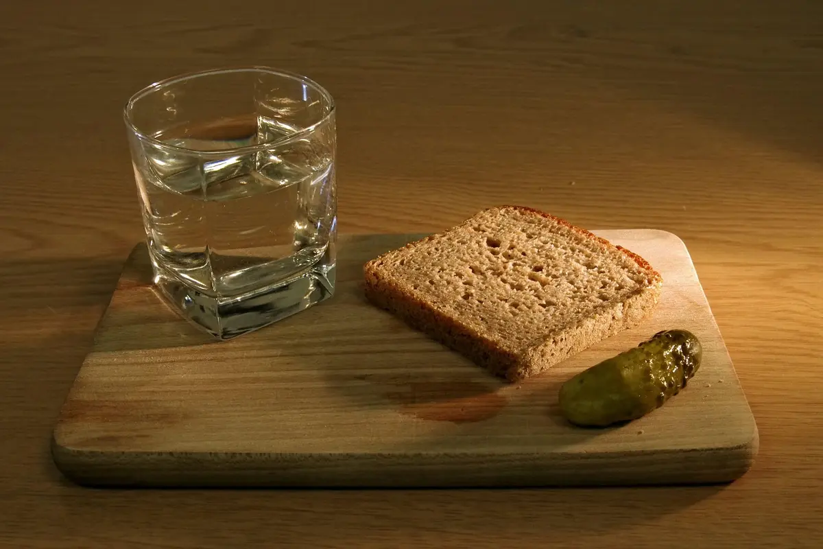 Glass of water on a wooden board with a slice of bread and a pickle