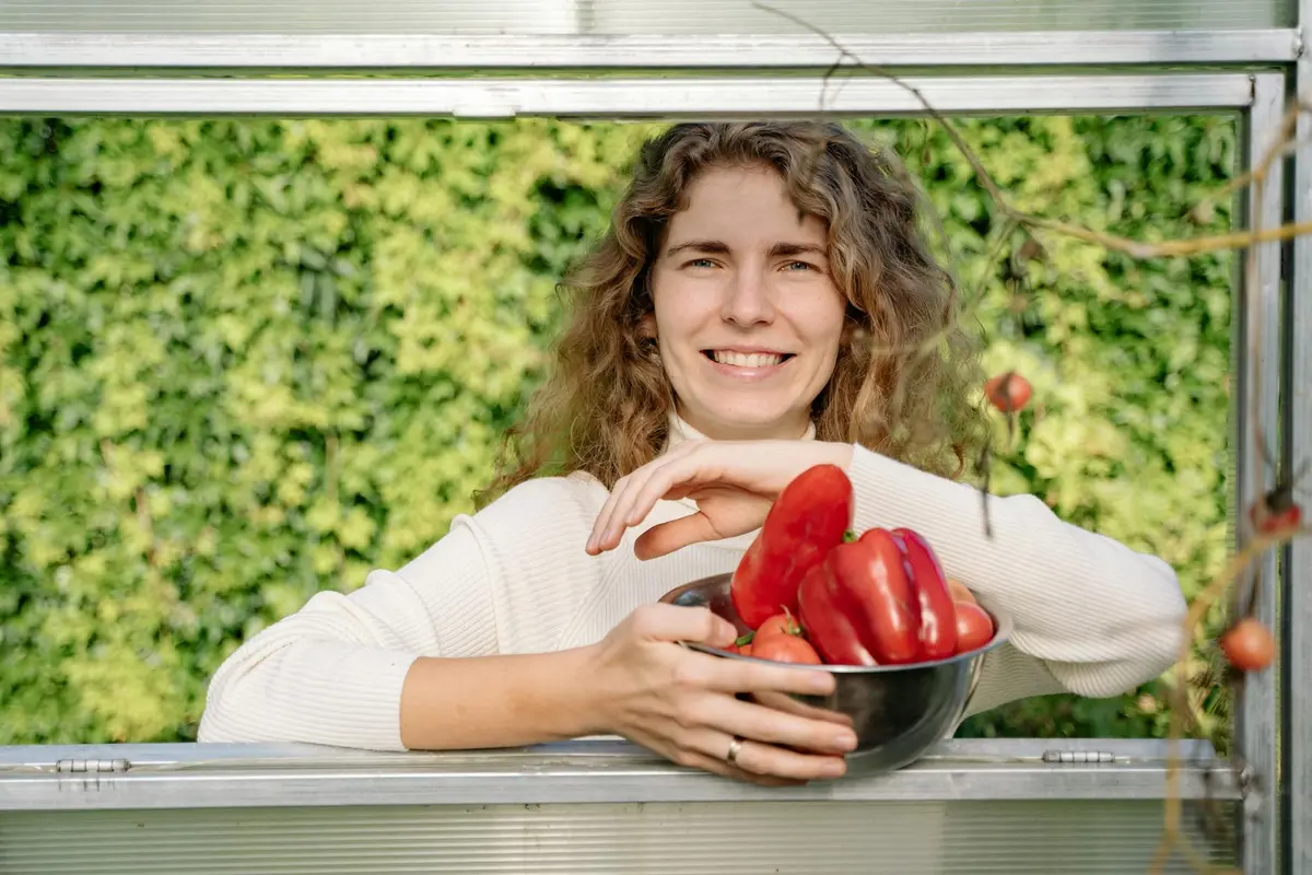 Smiling person holding a bowl of red bell peppers against a leafy green background