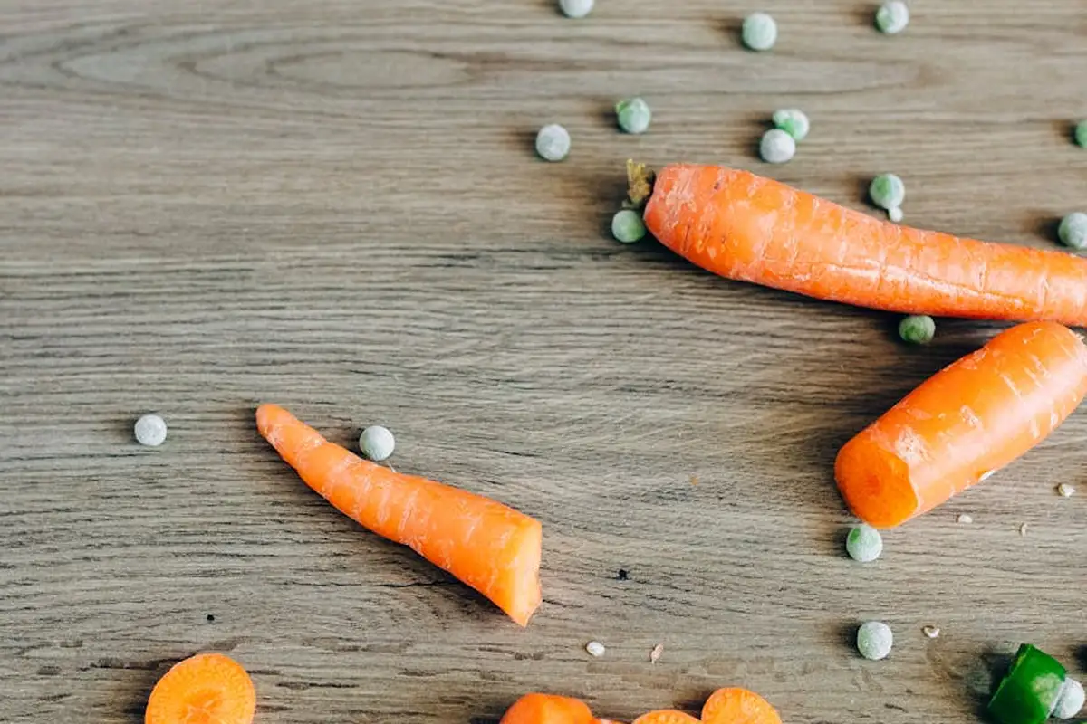 Carrots and peas scattered on a wooden surface, illustrating other veggie options for bearded dragons.
