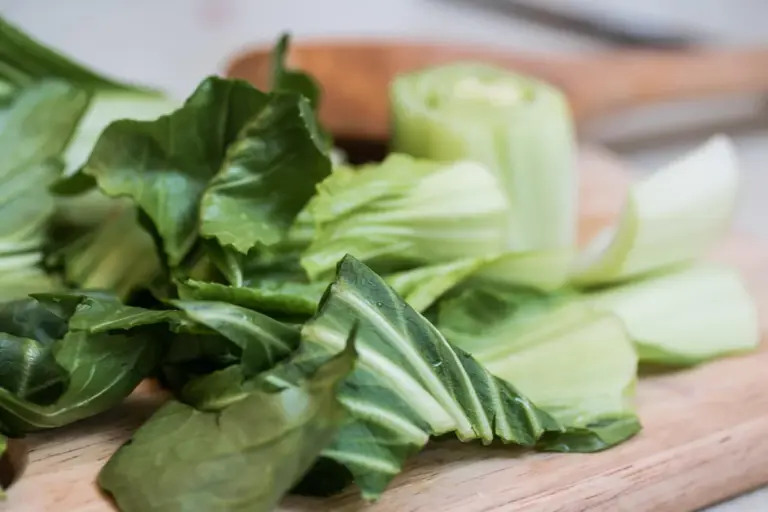 Fresh bok choy with dark green leaves and light green stalks on a wooden cutting board.
