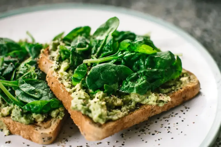 Two slices of toast topped with leafy greens on a plate, illustrating a serving of greens.