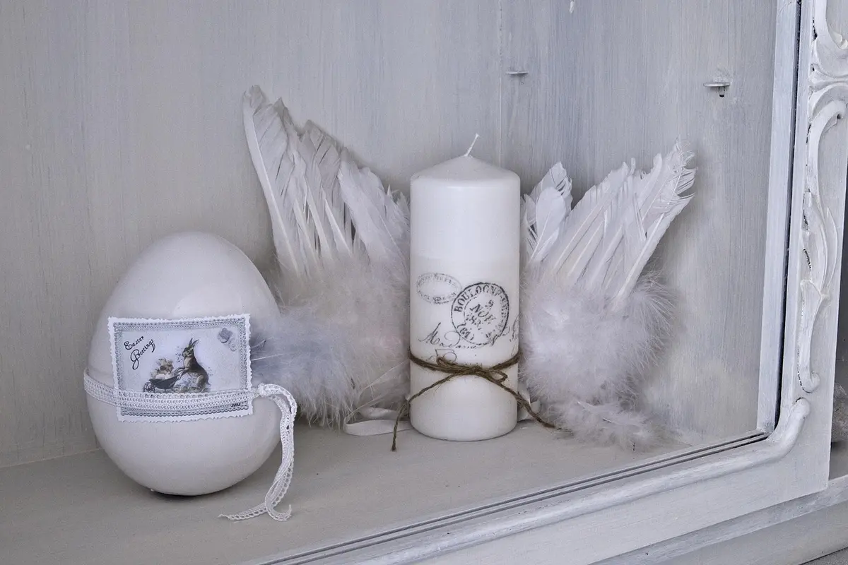 Decorative white eggs and a candle with feather accents on a shelf, illustrating egg care and viability considerations for bearded dragons.