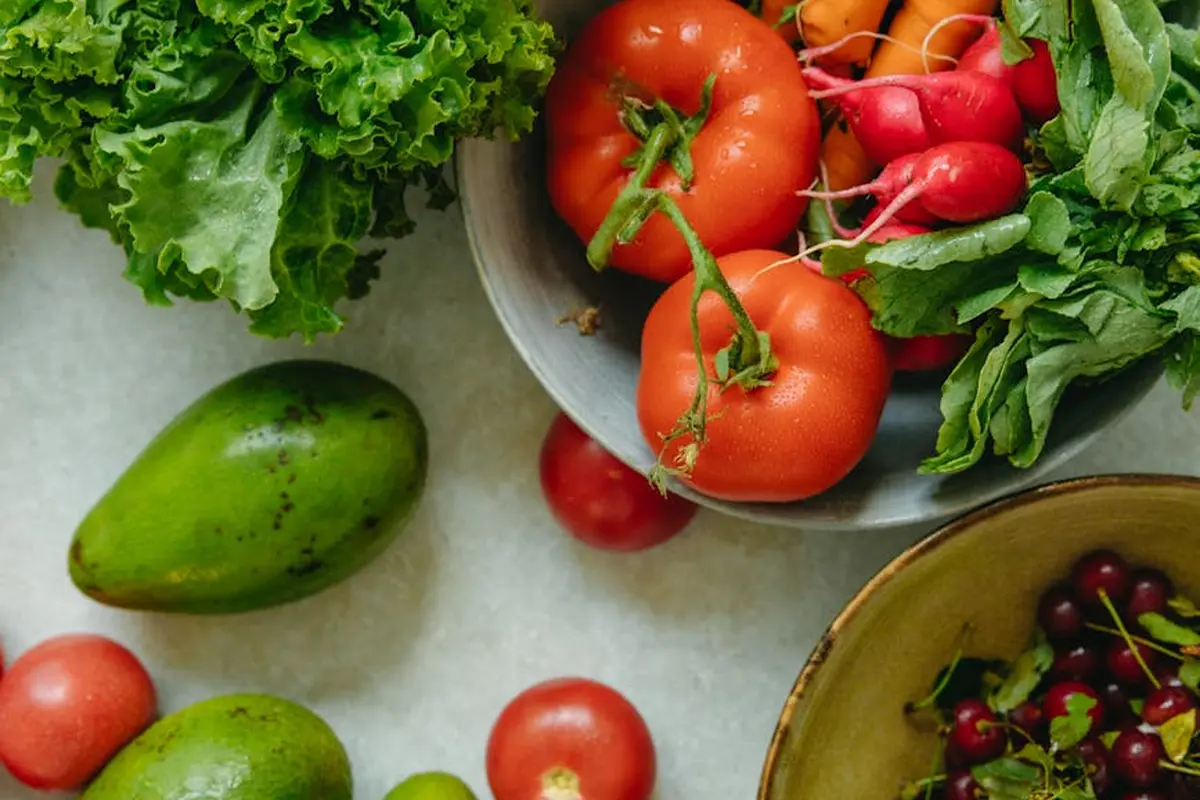 Assorted fresh greens and vegetables, including lettuce, tomatoes, radishes, and leafy greens on a light surface, illustrating colorful produce for a healthy reptile diet.