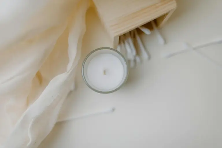 Close-up of a small white candle on a soft cream fabric background