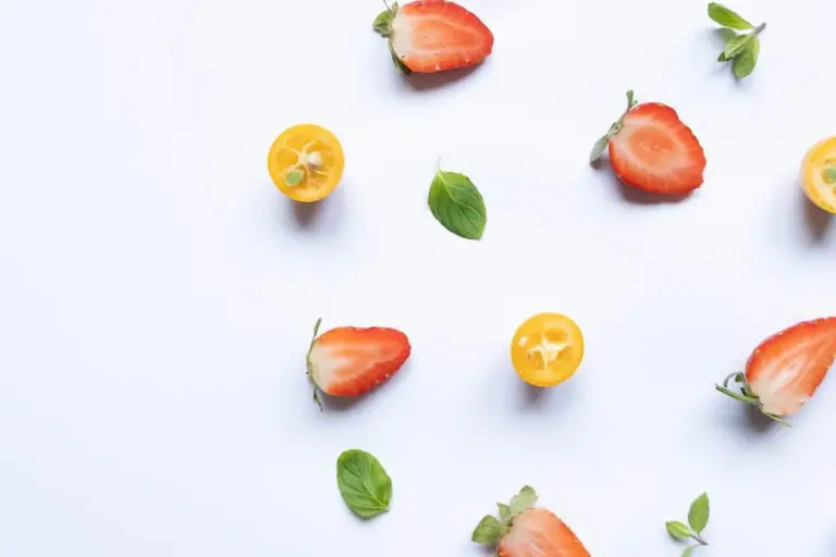 Assorted mint leaves and halved strawberries scattered on a white surface