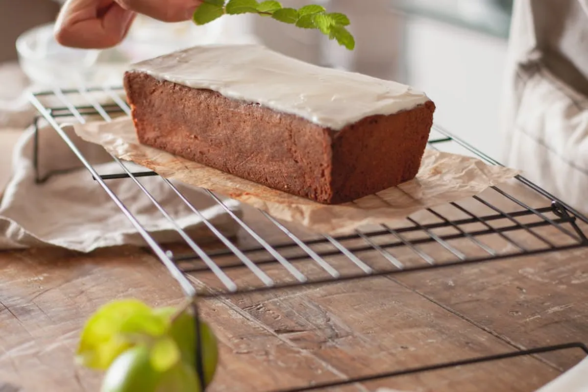 Fresh mint leaves being held over a cooled loaf on a wire cooling rack