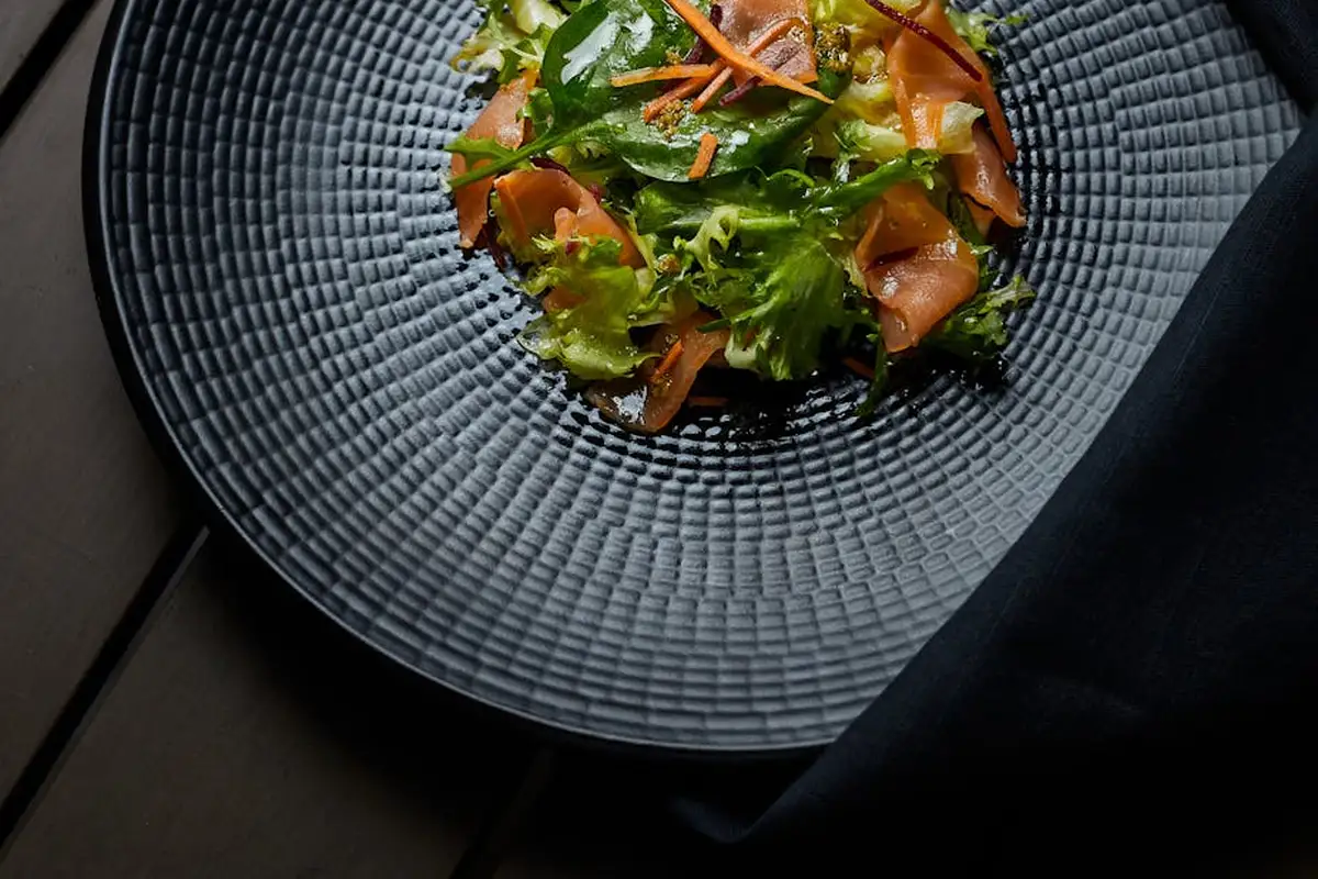 Plate of mixed leafy greens with shredded carrots on a textured blue-gray plate.
