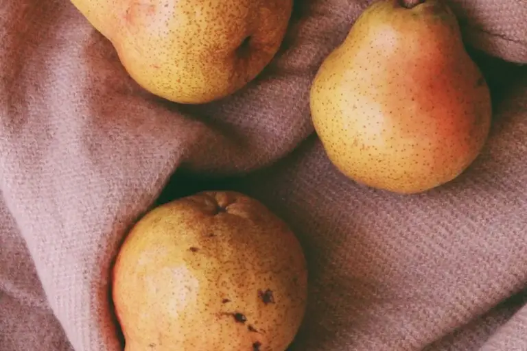 Three ripe pears resting on a soft pink fabric.