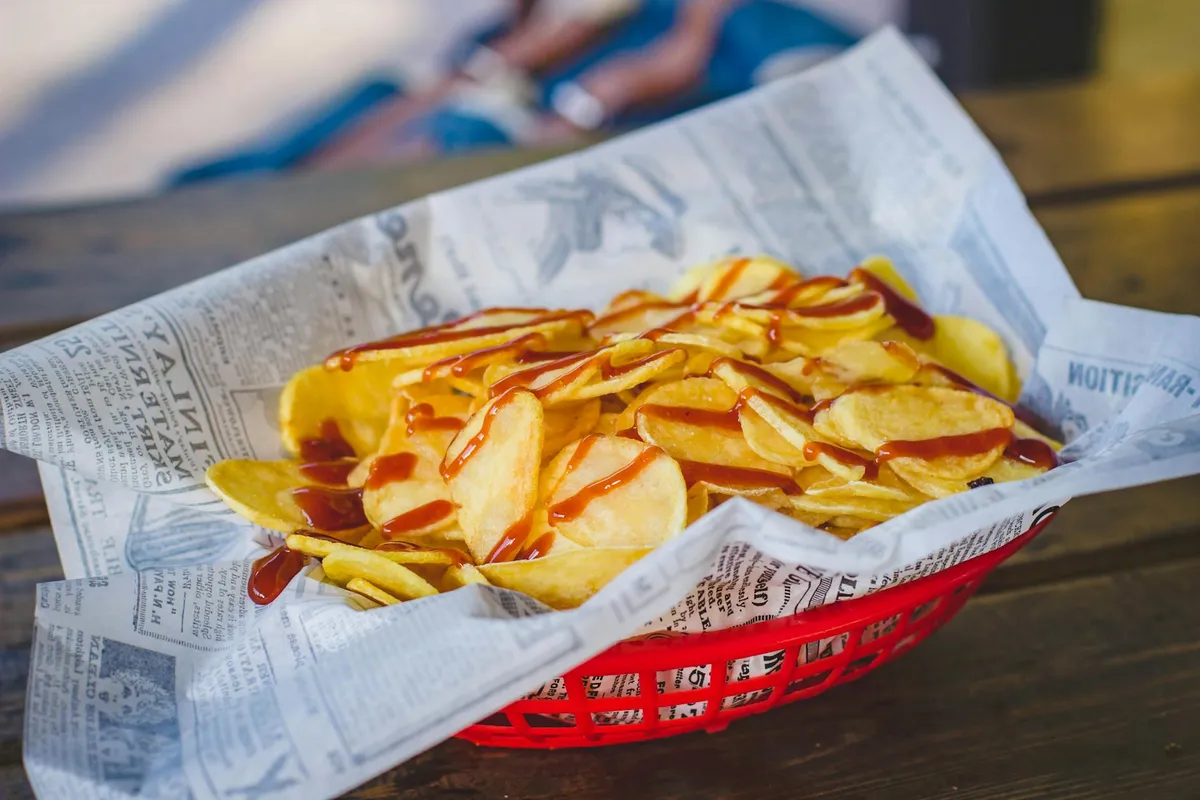 Basket of potato chips lined with newspaper on a wooden table.