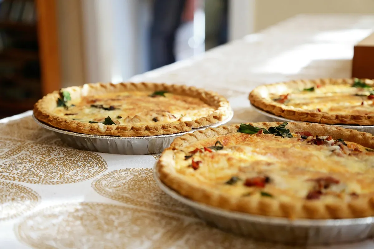 Three golden-brown quiche pies on a patterned tablecloth