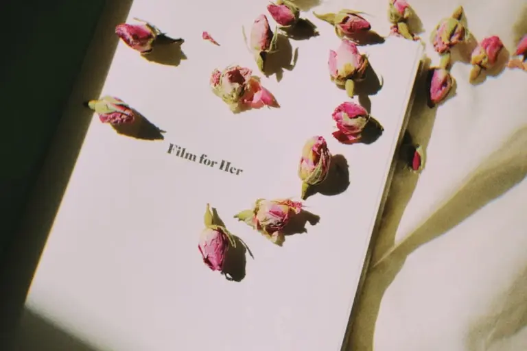 Rose petals and rosebuds scattered on a white surface with a page displaying the text 'Film for Her'.