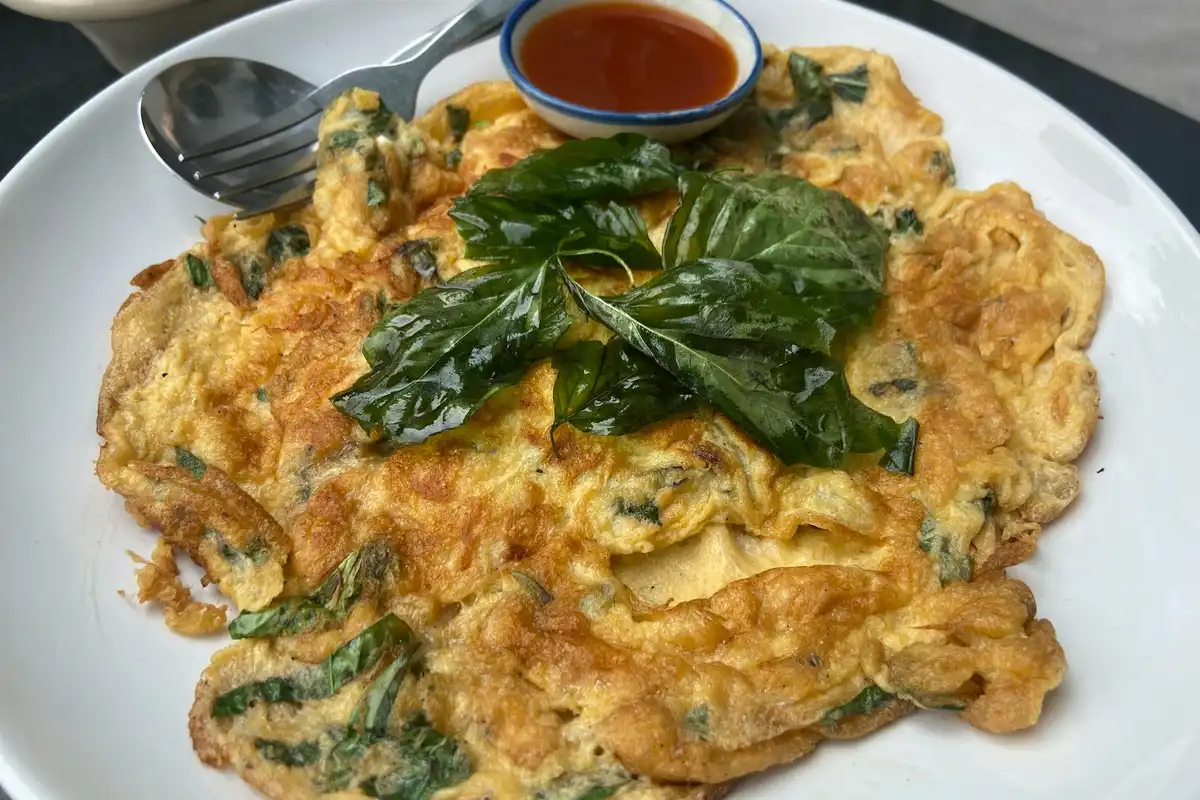 Omelette on a white plate topped with fresh spinach leaves and a small dipping sauce cup, with a fork nearby.