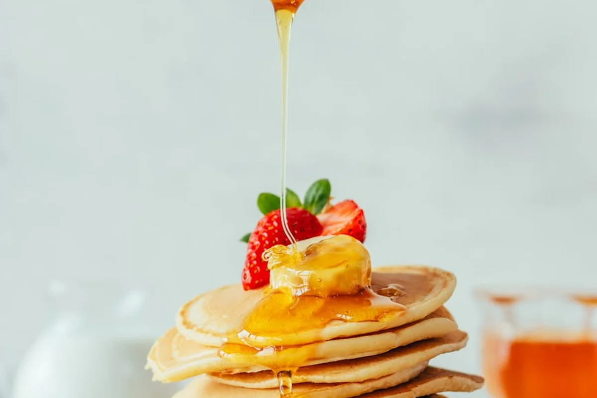 Stack of pancakes topped with a fresh strawberry, with honey being drizzled over them.
