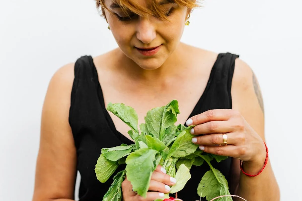 Person with short hair wearing a black top holding fresh turnip greens, looking at the leaves