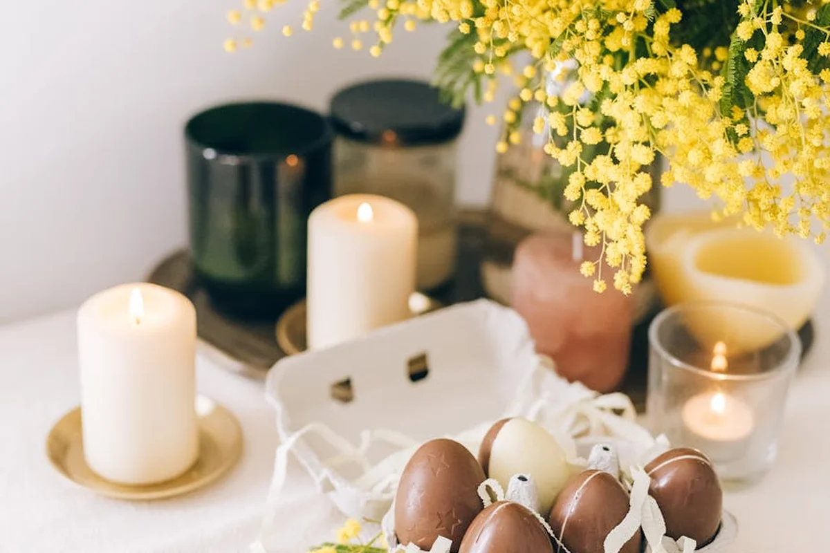 Decorative nest of Easter eggs with candles and yellow flowers on a white surface