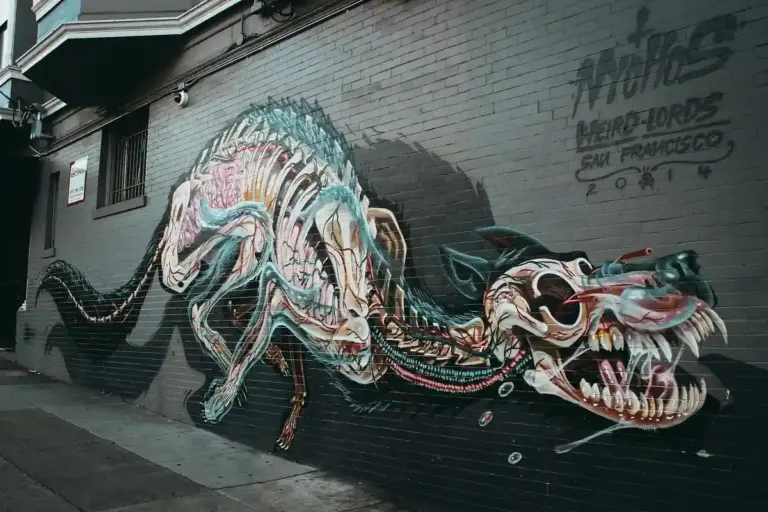 Colorful dragon mural painted on a brick wall beside a sidewalk in an urban alley.