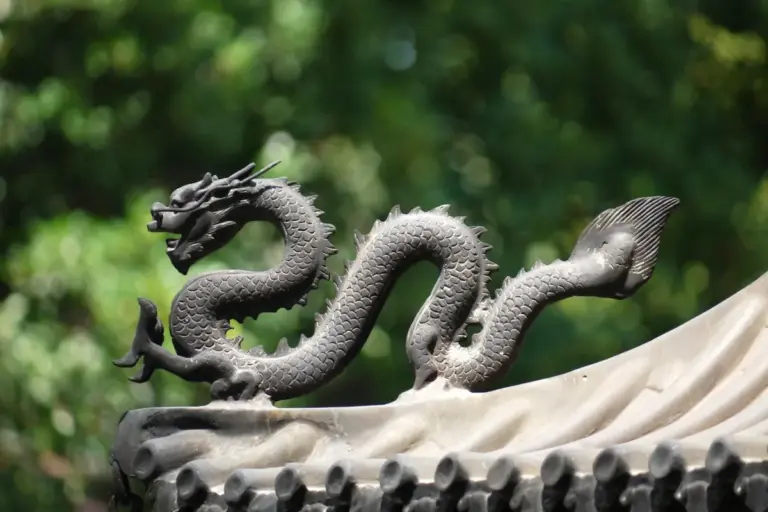 Decorative dragon sculpture with two heads along a tiled roof, outdoors with a blurred green background.