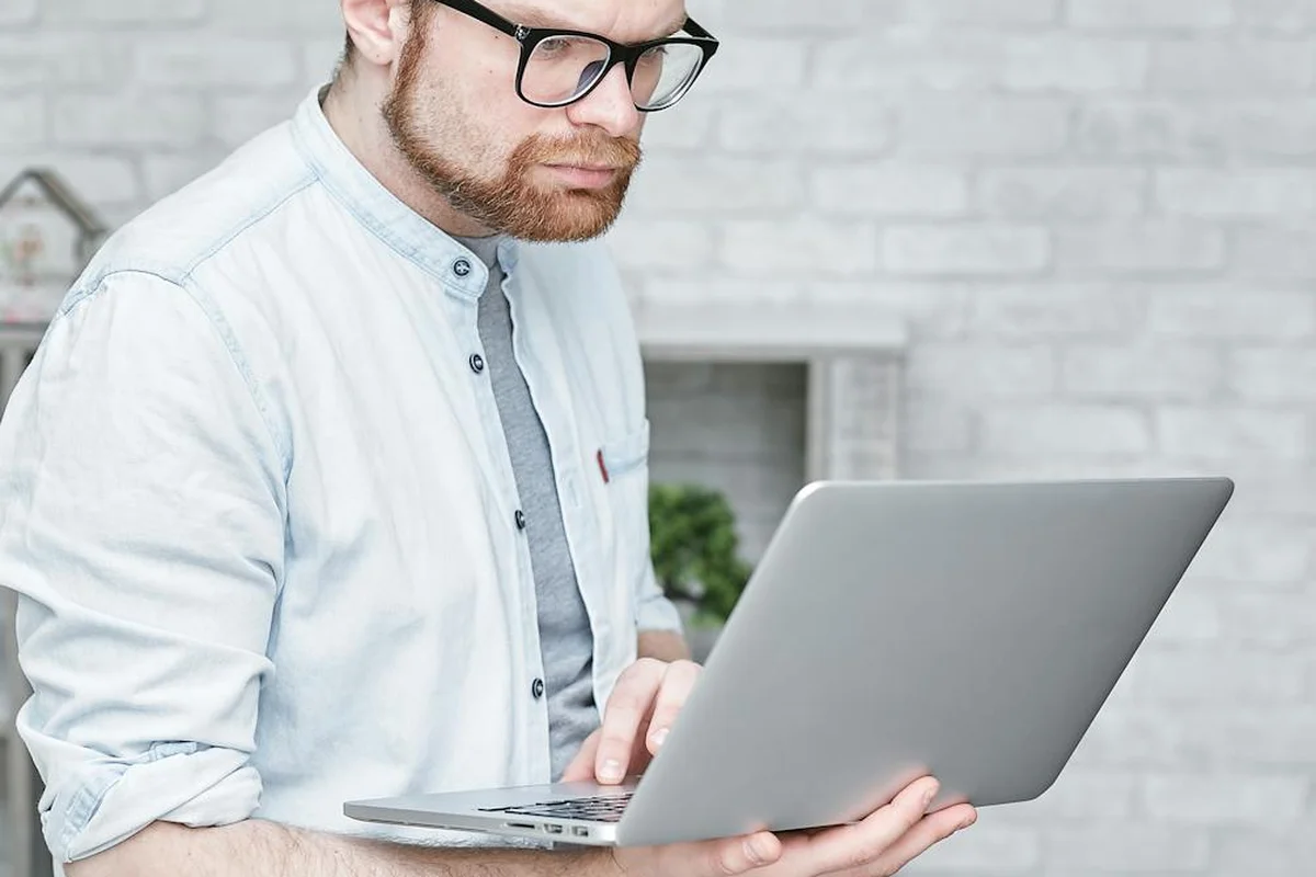 Man wearing glasses and a light shirt typing on a laptop, researching laws about bearded dragon ownership